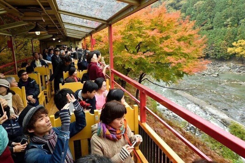 People seated on yellow benches on a covered walkway overlooking a river. 4