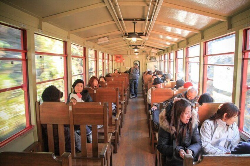 A train interior with passengers seated, wooden benches, and large windows. 3