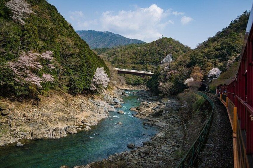 A train traveling through a mountainous area with a river, greenery, and a bridge. 2