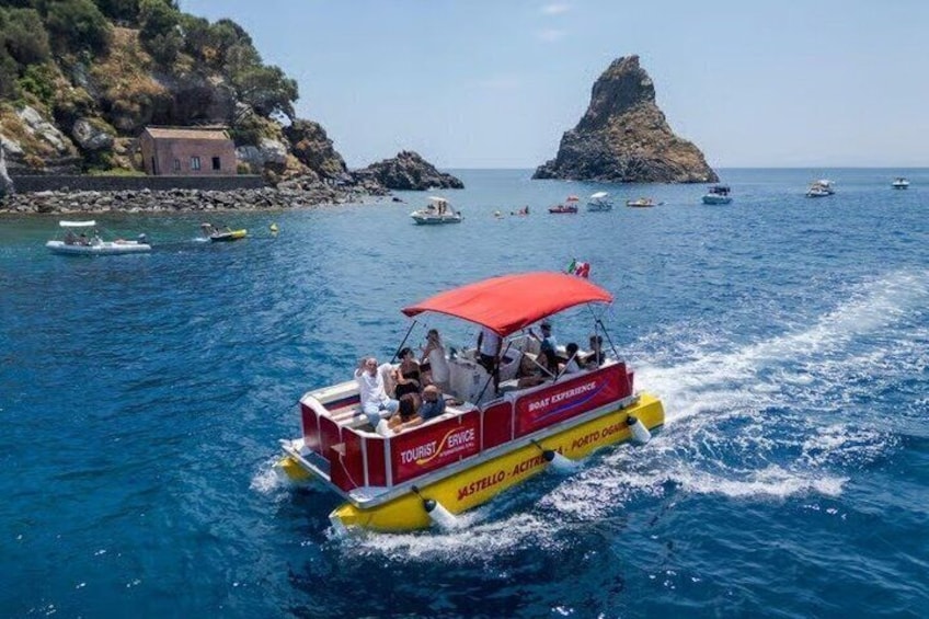 Een rode en gele boot met passagiers, glijdend door helderblauw water, met rotsachtige landtongen en boten op de achtergrond. 3
