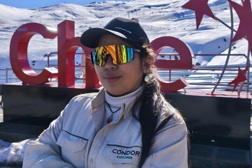Une personne portant une veste « CONDOR EXPLOVER » est assise devant un grand panneau rouge avec les lettres « CH », sur fond de montagne enneigée. 5