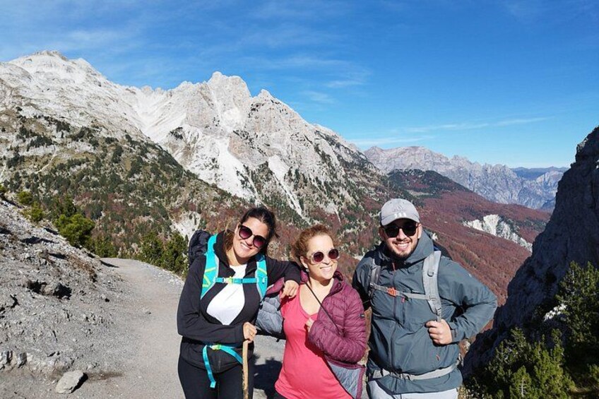 Three people hiking on a mountain trail with rocky terrain and mountains in the background. 5