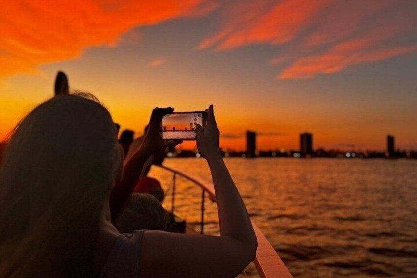 Iemand maakt een foto van een zonsondergang boven het water, met gebouwen op de achtergrond. 5