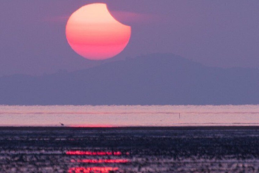 Een zonsondergang boven een wateroppervlak, met bergen op de achtergrond. 2