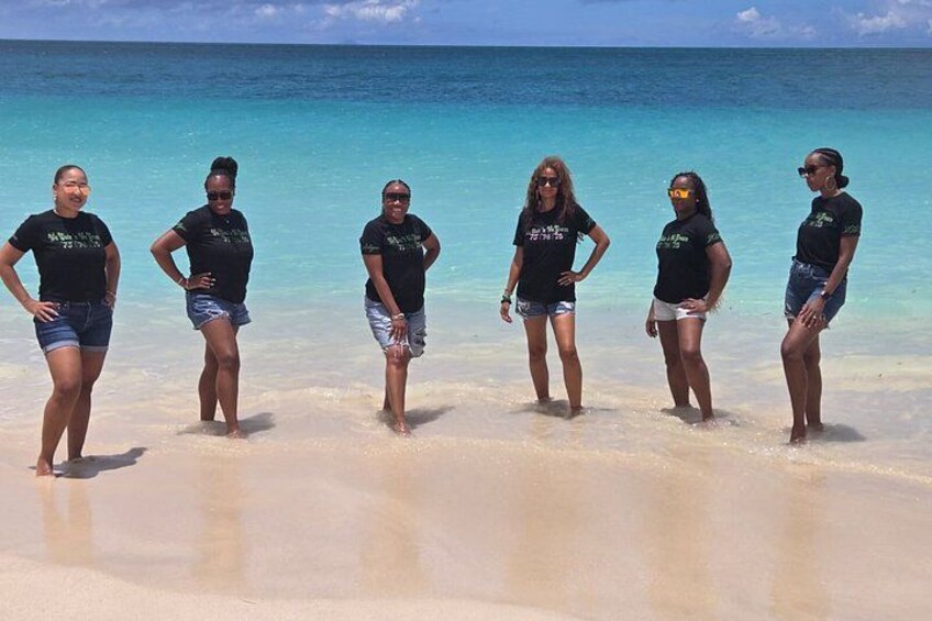 Un grupo de personas de pie en una playa con aguas azules y cristalinas al fondo. 1