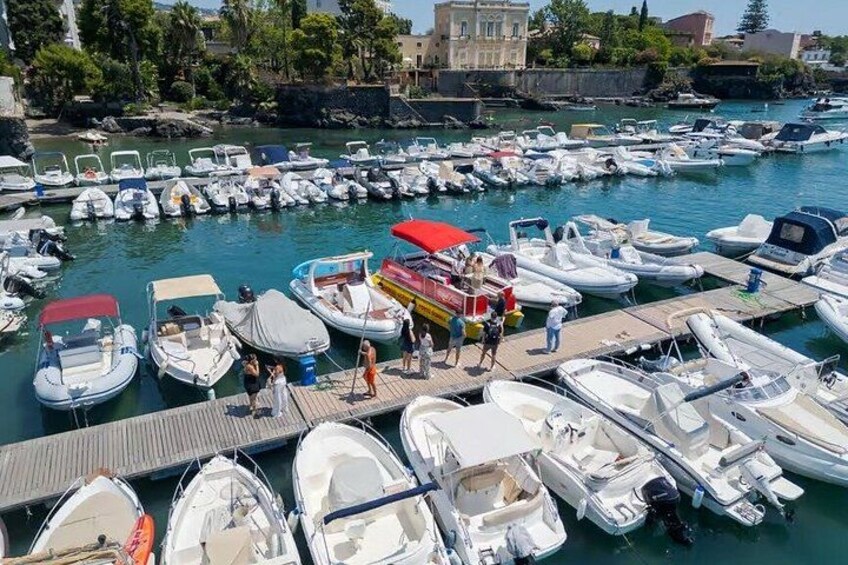 Una marina con numerose imbarcazioni ormeggiate, una piccola barca con persone sul molo e edifici sullo sfondo. 2