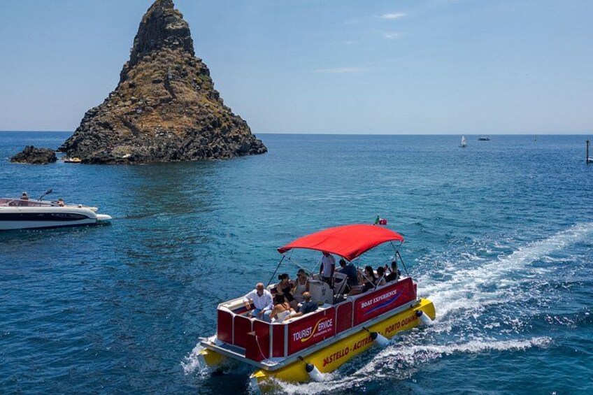 Una barca rossa con una tenda da sole, chiamata 'ASTELLO-ACTUAL', che scivola sull'acqua con un'isola rocciosa sullo sfondo. 1