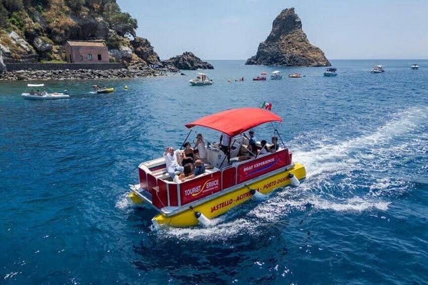 Una barca rossa e gialla con turisti su un mare blu limpido, circondata da isole rocciose e altre imbarcazioni. 3