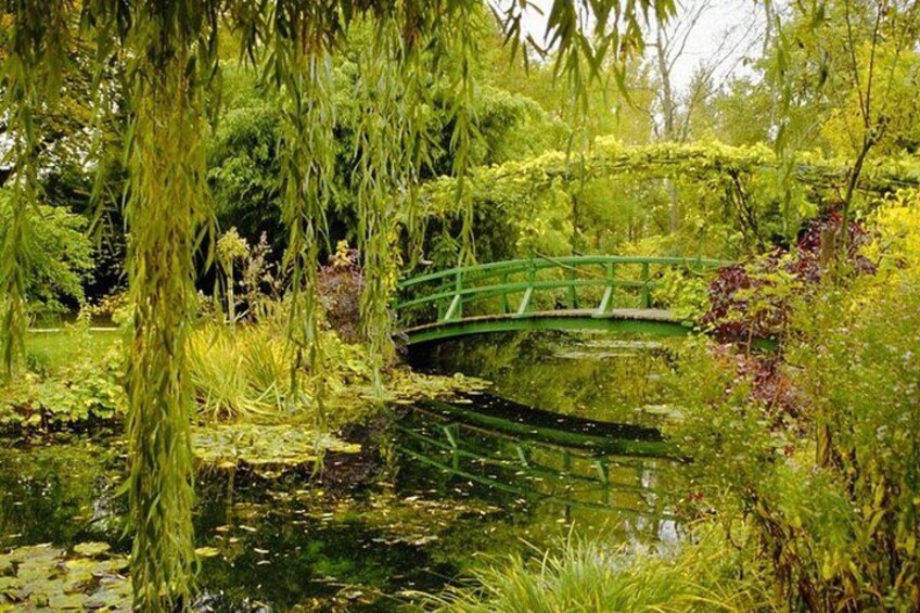 A tranquil pond with a green bridge, surrounded by lush greenery and various plants. 3