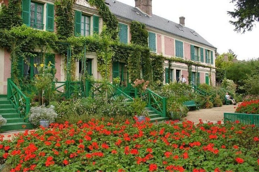 A house with green shutters and a garden with red flowers. 2