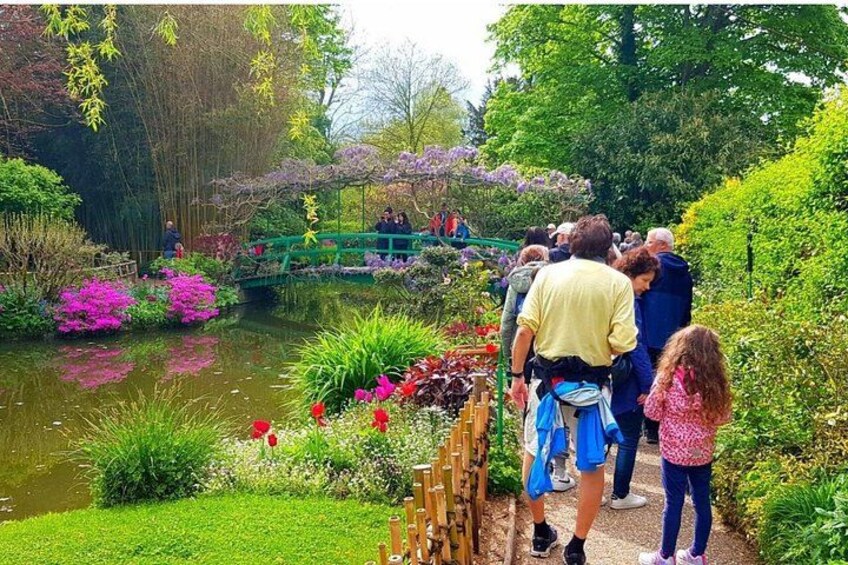 A garden with a pond, a bridge, and people walking. 1