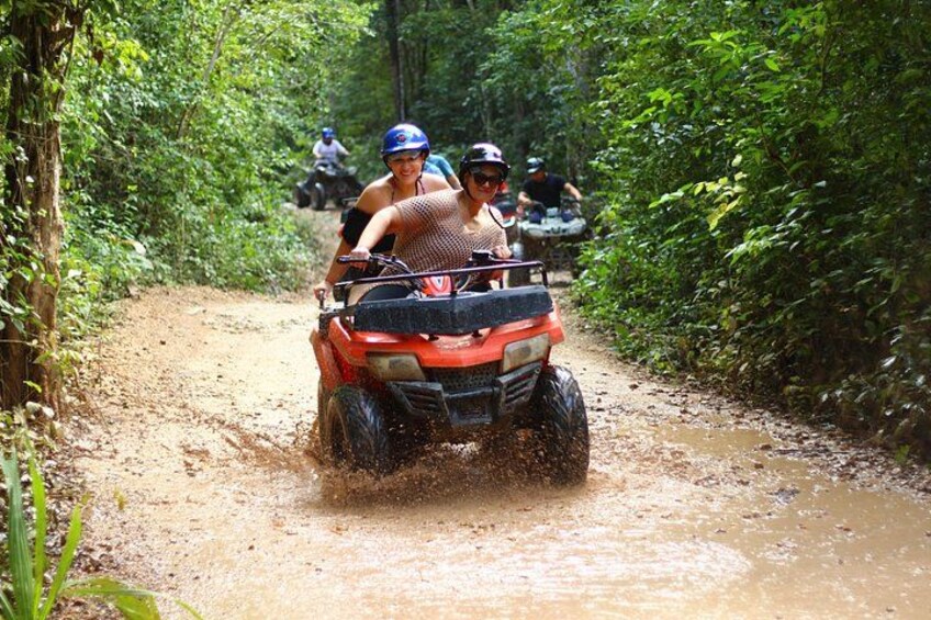 A person riding an ATV on a muddy path surrounded by dense greenery. 3