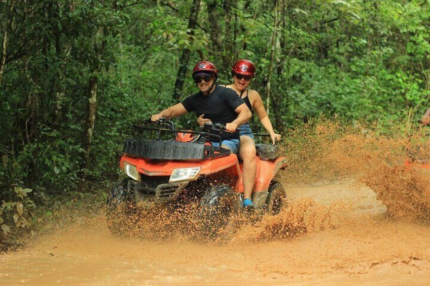 Two people on an ATV in a forested area. 1