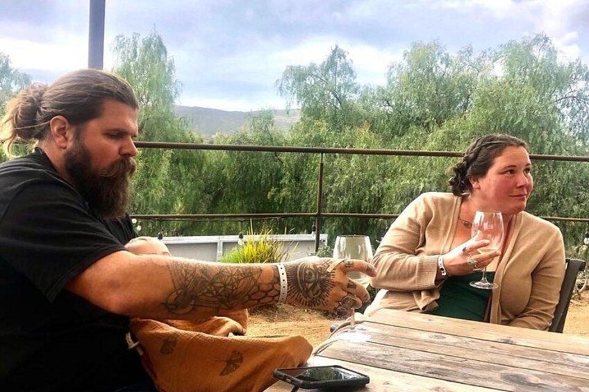Two people sitting at a table outdoors with a view of trees and hills in the background. 3