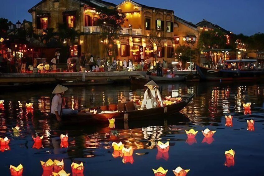 A traditional boat with a person wearing a conical hat on the water, a building with illuminated windows, and floating lanterns. 2