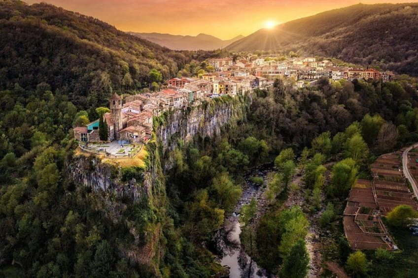 A town perched on a cliff overlooking a river, surrounded by forested hills. 1