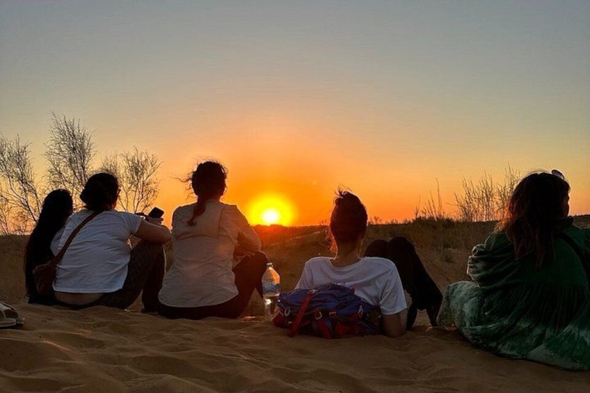 Ein Sonnenuntergang über einem Sandstrand, auf dem Menschen sitzen und zusehen. 2