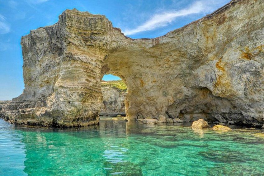 A natural rock formation with a cave-like arch over clear turquoise water. 3