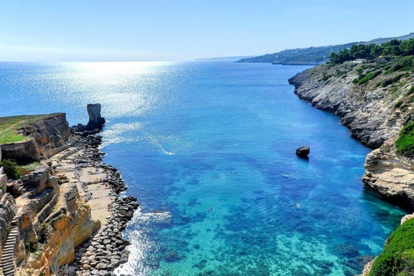 A coastal landscape with cliffs, clear blue sea, and a rocky shoreline. 2