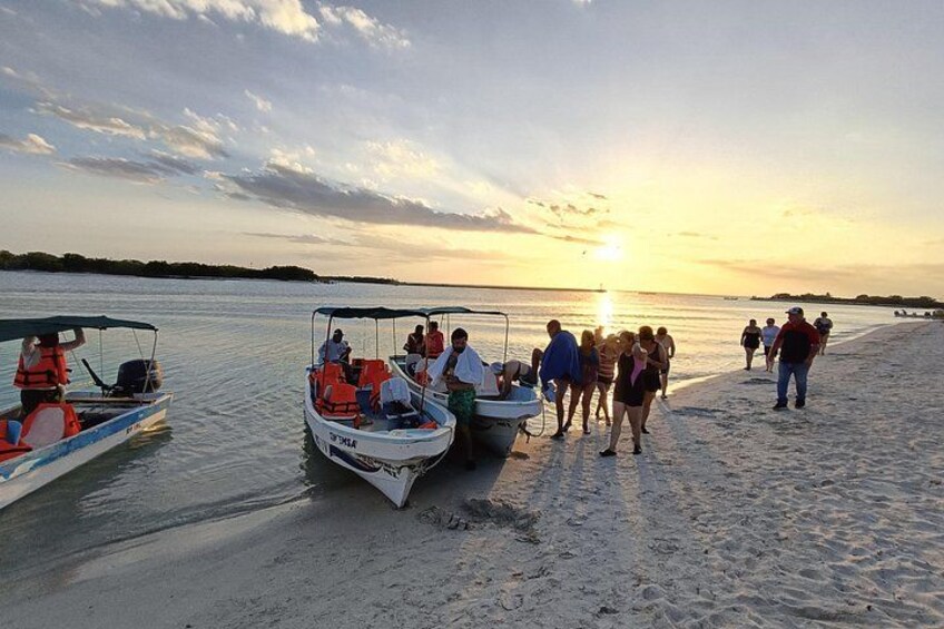 Un coucher de soleil sur une plage, avec des personnes et des bateaux. 2