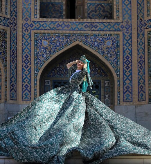 A person in traditional attire in front of a building with intricate blue and beige tile patterns. 3