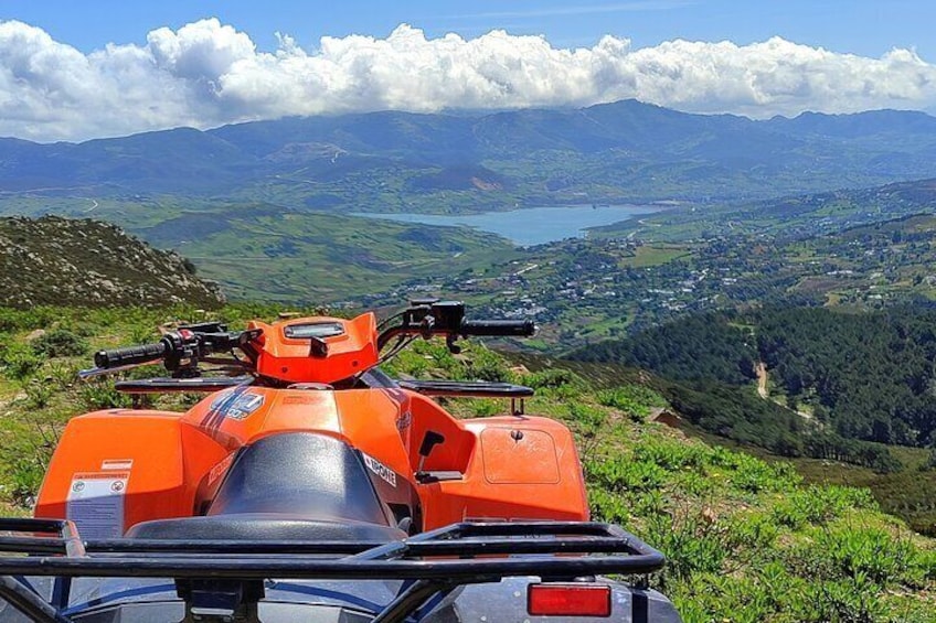 Un quad orange est garé sur une colline herbeuse, d’où l’on a une vue sur une vallée, des montagnes et un lac. 5