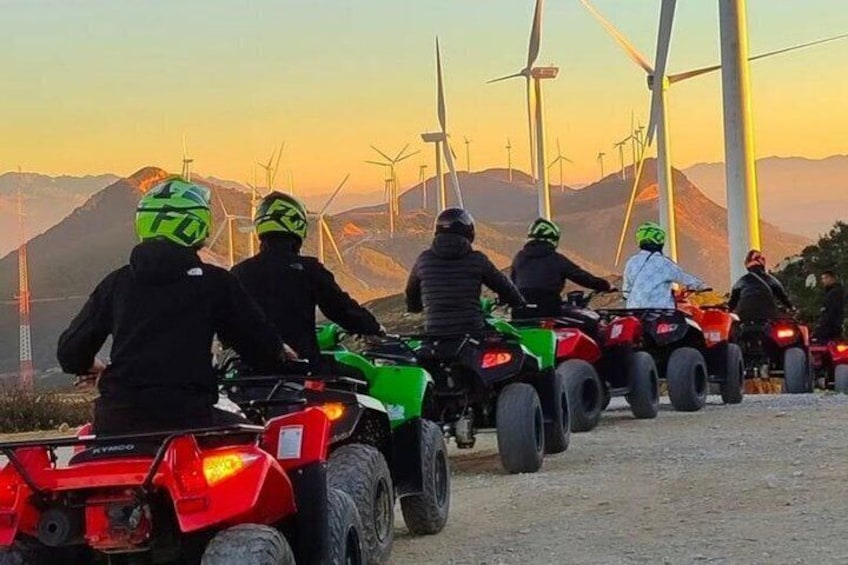 Un groupe de personnes circulant en quads dans une région montagneuse, avec des éoliennes en arrière-plan. 1