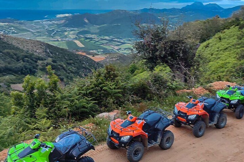 Quatre quads sont stationnés sur un chemin de terre, offrant une vue panoramique sur les montagnes et les vallées. 4