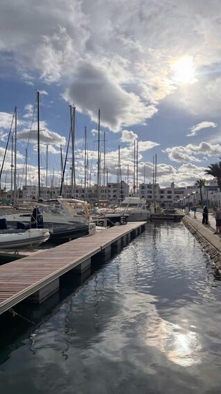 A marina with multiple sailboats docked along a wooden pier, under a partly cloudy sky. 5