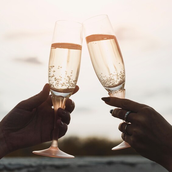 Two hands holding champagne flutes with bubbles, against a blurred background. 3