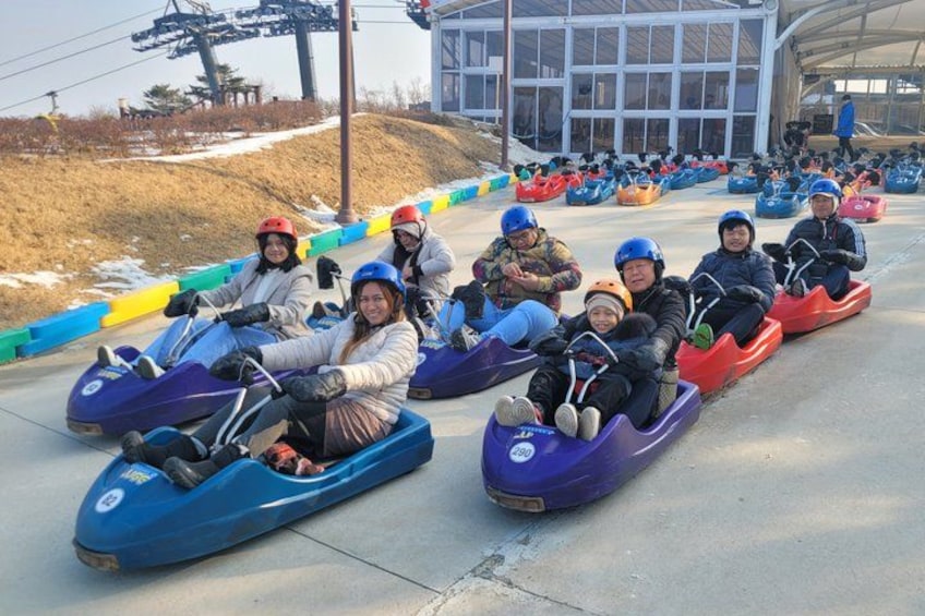 People in go-karts on a track with a building in the background. 2