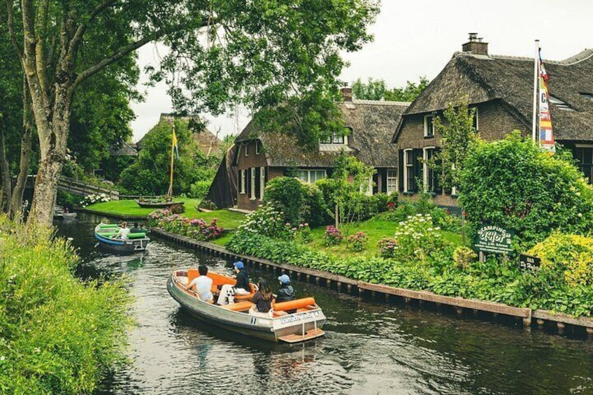 A narrow canal with a boat, houses with thatched roofs, and lush greenery. 3