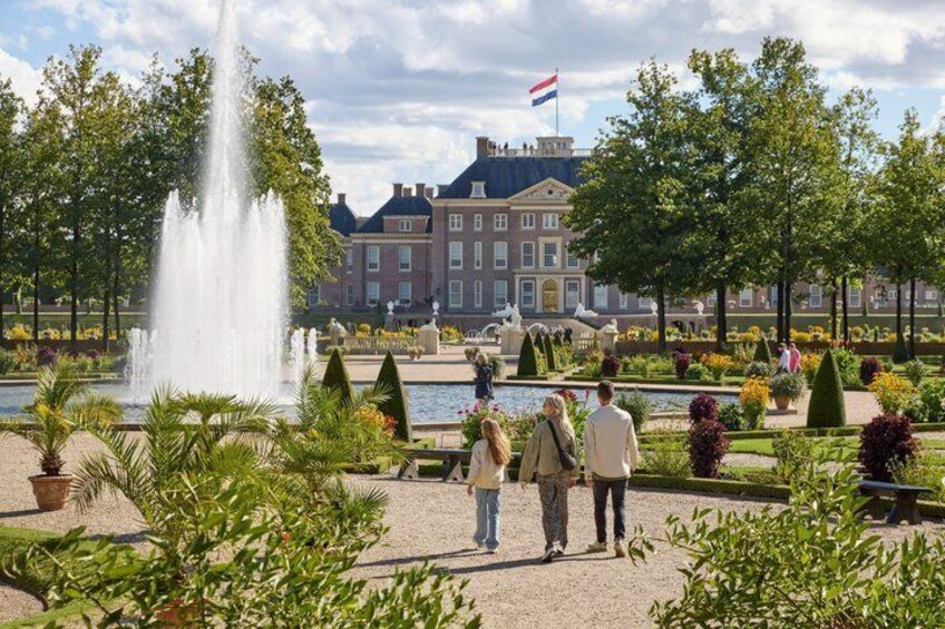 A fountain, a large building with a flag, and people walking in a garden. 5