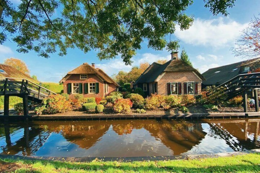 A canal with two traditional houses, a wooden bridge, and a pond reflecting the buildings. 2