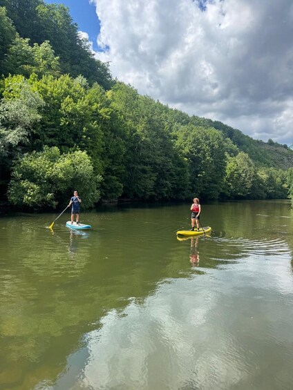 Two people paddleboarding on a calm river surrounded by dense green forest and hills. 3