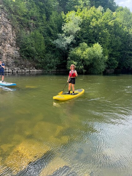 A person paddleboarding on a river surrounded by dense green foliage. 4