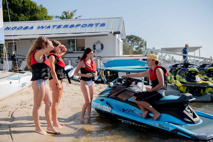 A group of people on a beach near a watersports facility with a jet ski. 5