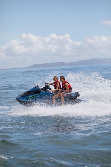 Two people jet-skiing on a body of water with a mountainous landscape in the background. 1