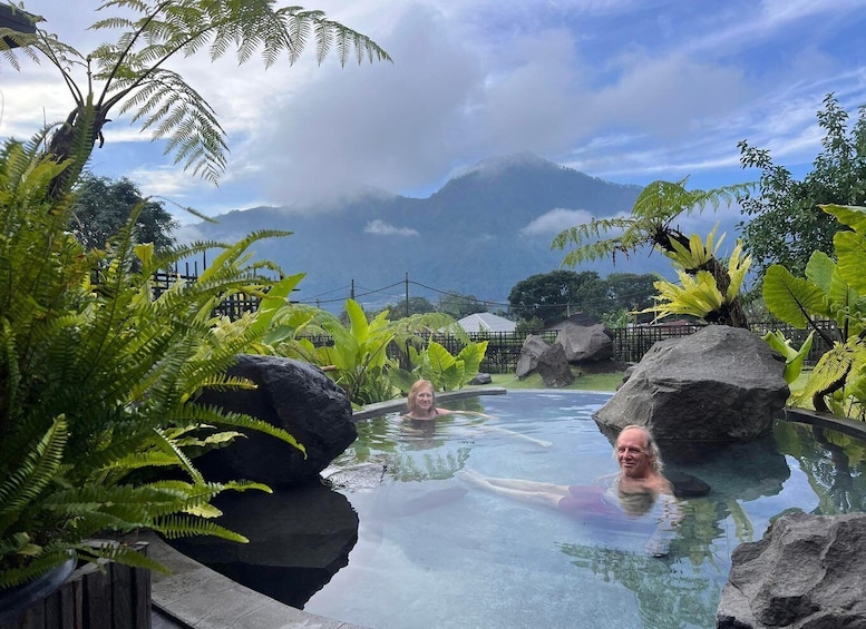 A man and a woman in a natural pool surrounded by tropical plants and rocks. 1