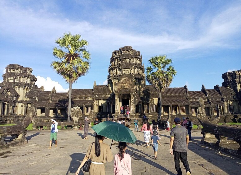 A historic temple complex with visitors and palm trees. 4