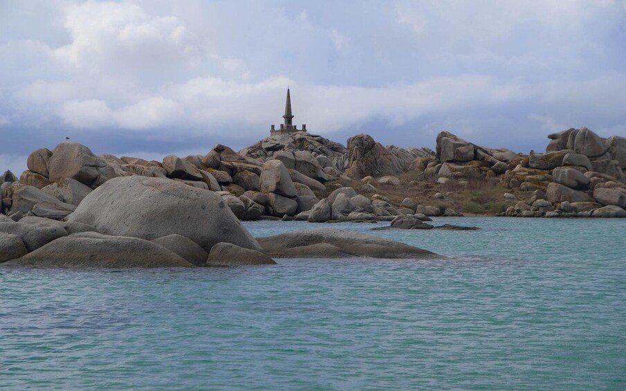 A rocky coastline with large boulders and a small monument. 5