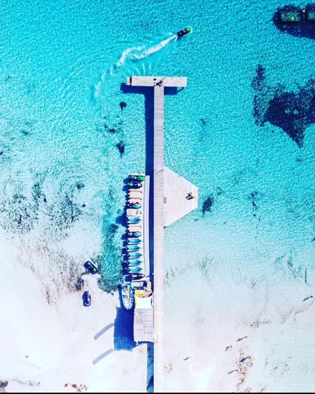 An aerial view of a pier extending into turquoise water, with several boats docked and a person swimming. 4