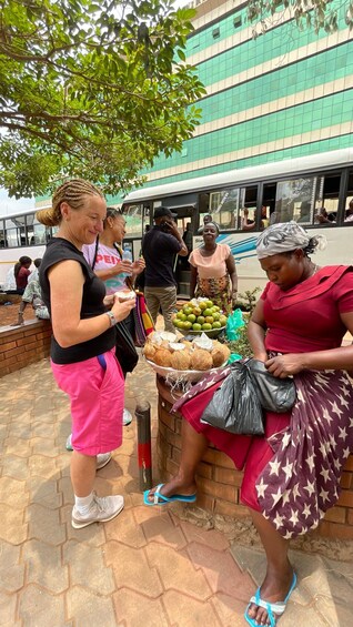 A street vendor selling coconuts and fruits, with a bus and people in the background. 2