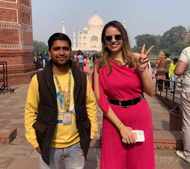 Two people standing in front of the Taj Mahal with the monument in the background. 1