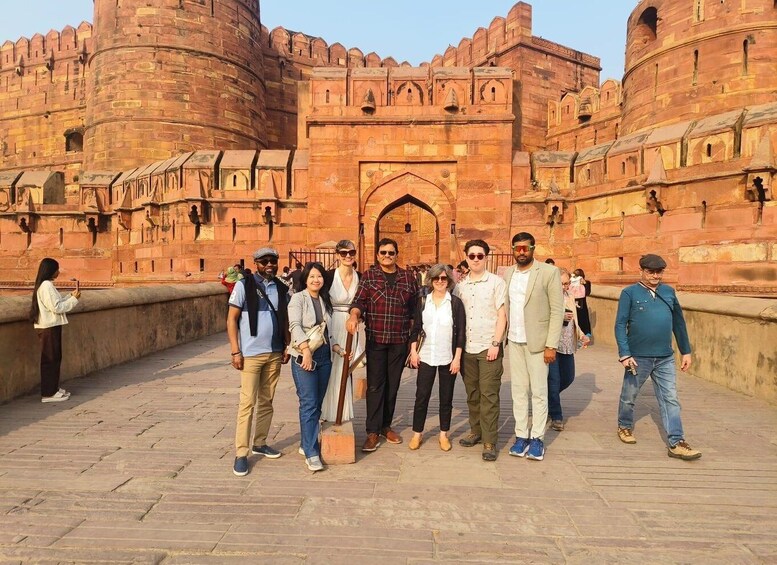 A group of people standing in front of a large, historic red stone fort with multiple arches and battlements. 2