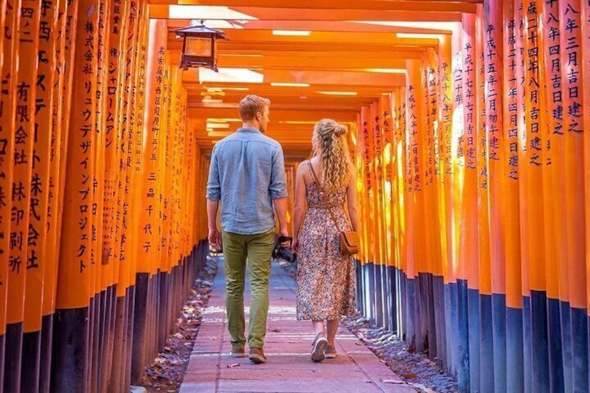 A couple walking through a corridor lined with orange torii gates. 1