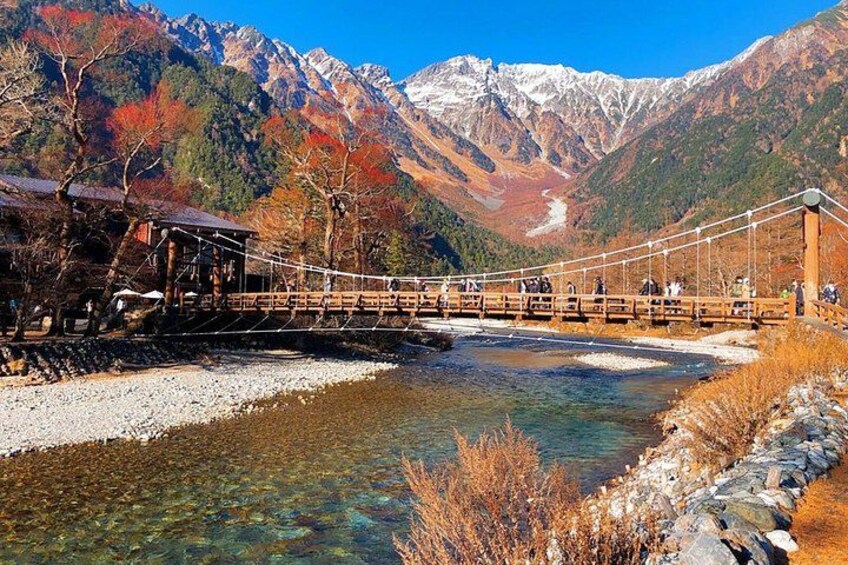 A suspension bridge over a river, surrounded by mountains and autumn foliage. 1