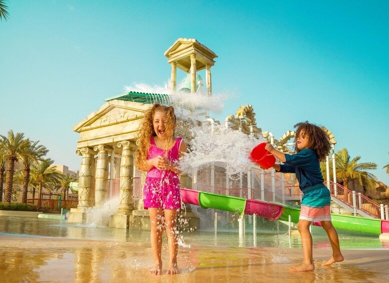 Two children playing in a water park with a water fountain and palm trees in the background. 2