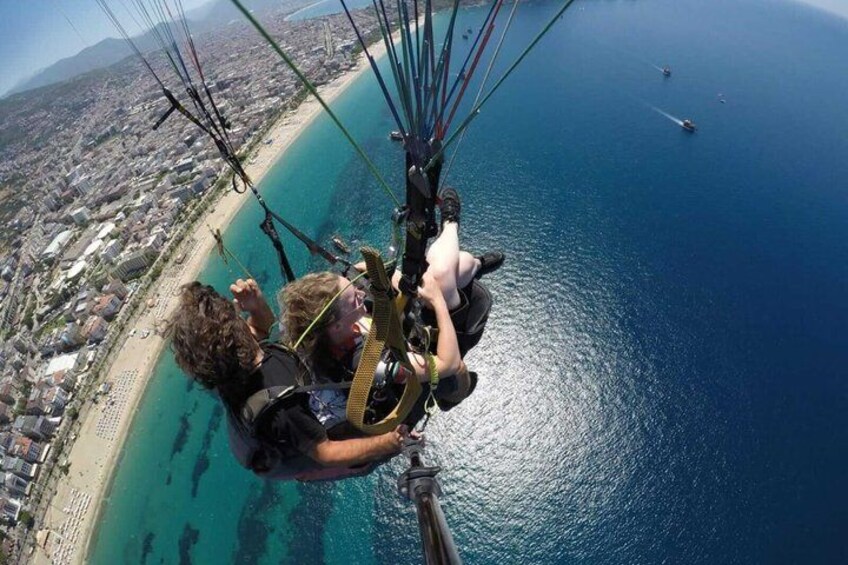 En tandem-paragliding aktivitet over et kystområde med en strand og klart, blåt vand. 2