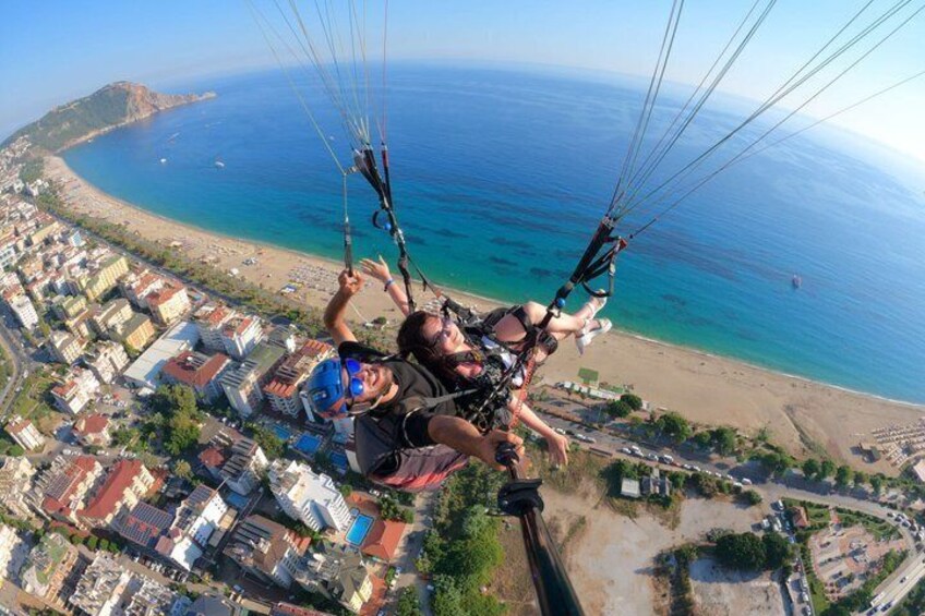En person paraglider over et kystområde med bygninger og en strand nedenfor. 4